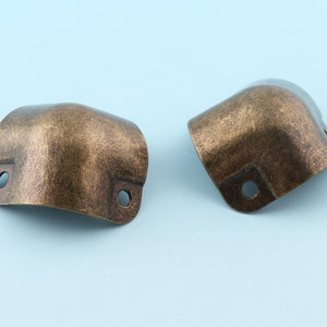 Op de afbeelding: Twee antieke gouden hoekbeschermers met een verweerde afwerking. Elke beschermer heeft twee gaten om te bevestigen aan meubels.