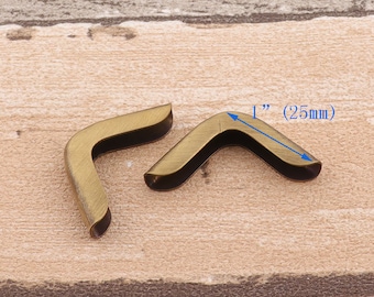 May include: Two antique gold metal corner protectors, each measuring 1 inch (25 mm) in length. The corner protectors are designed to protect the edges of leather goods, such as books, journals, and photo albums.