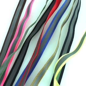 Pode incluir: Conjunto de fitas reflexivas em várias cores, incluindo preto, marrom, verde, vermelho, azul, amarelo e rosa. Cada fita tem uma faixa reflexiva que percorre o centro.