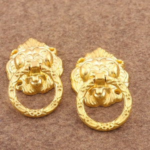 May include: Two gold lion head door pulls with ornate details and a ring handle.