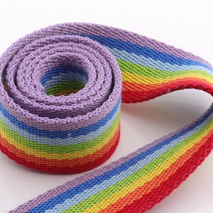 May include: A rainbow striped woven webbing with a purple base color. The webbing is rolled up and the stripes are visible in the roll.