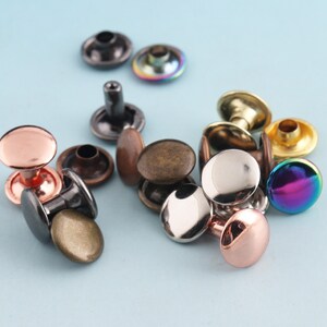 May include: Assortment of metal rivets in various colors, including silver, gold, copper, rose gold, and iridescent. The rivets are round and have a flat top with a raised center.