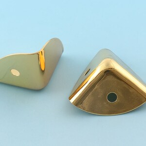 May include: Two gold metal corner protectors with a rounded edge and a hole in the center.
