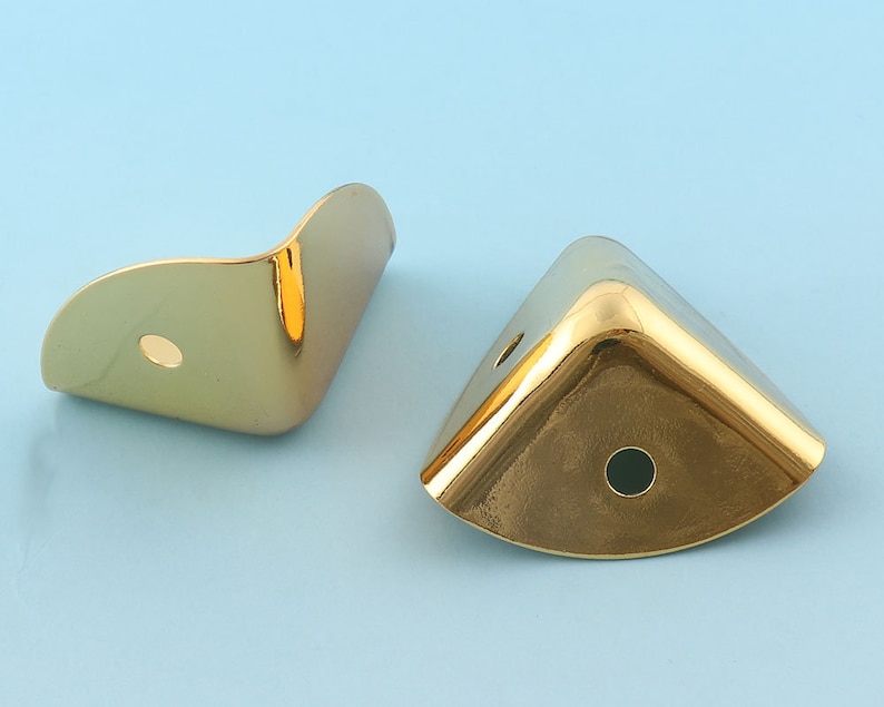 May include: Two gold metal corner protectors with a rounded edge and a hole in the center.