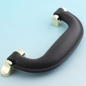 May include: Black plastic handle with gold metal accents. The handle has a textured surface and is designed for carrying.