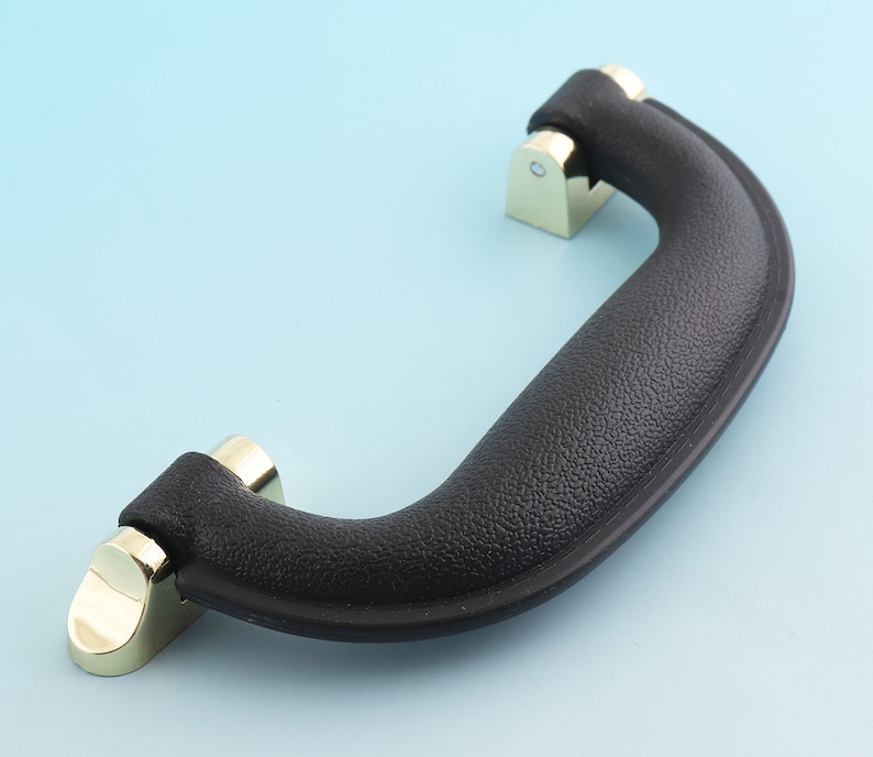 May include: Black plastic handle with gold metal accents. The handle has a textured surface and is designed for carrying.