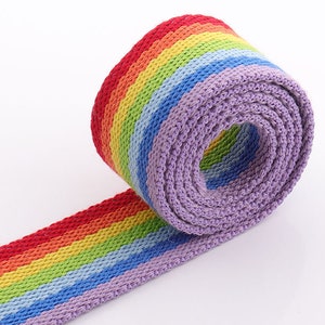May include: A rainbow colored woven webbing with a purple backing. The webbing is rolled up and the rainbow colors are visible on the outside of the roll.