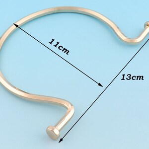 May include: A gold-toned metal bangle bracelet with a curved design. The bracelet measures 11 cm in diameter and 13 cm in length.
