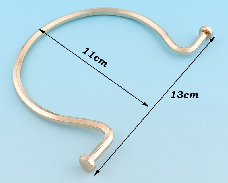 May include: A gold-toned metal bangle bracelet with a curved design. The bracelet measures 11 cm in diameter and 13 cm in length.