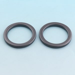 Puede incluir: Dos anillos de metal negro, cada uno con una superficie lisa y redondeada. Los anillos tienen un di&aacute;metro de aproximadamente 5 cm y son ideales para sujetar a bolsos, cinturones u otros accesorios.