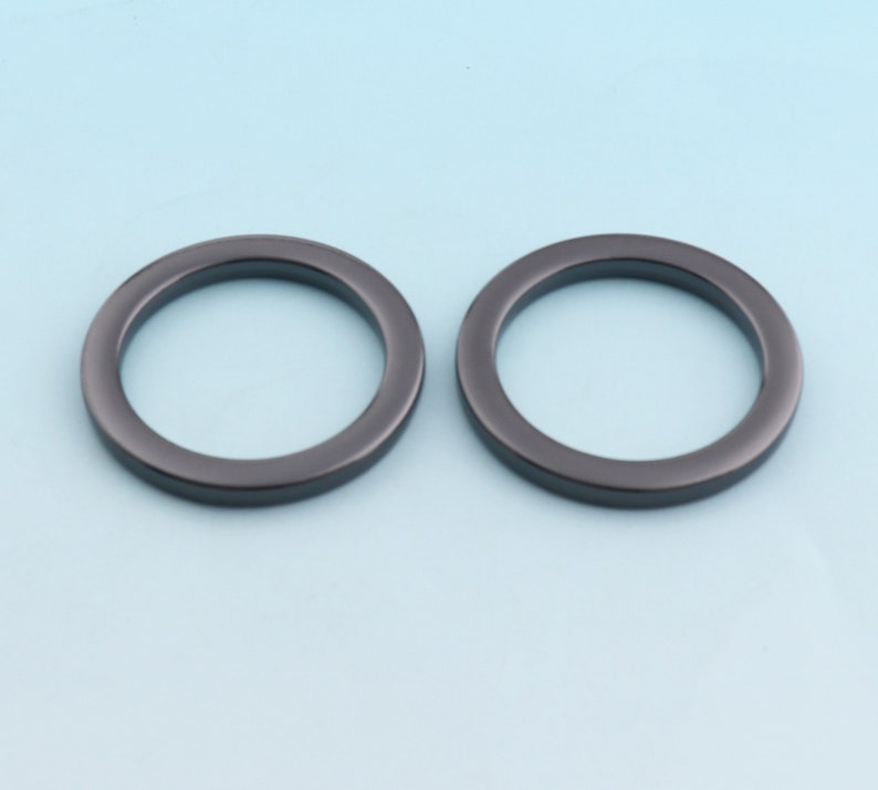 Puede incluir: Dos anillos de metal negro, cada uno con una superficie lisa y redondeada. Los anillos tienen un di&aacute;metro de aproximadamente 5 cm y son ideales para sujetar a bolsos, cinturones u otros accesorios.