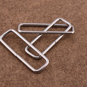 May include: Three silver metal rectangular rings, stacked on top of each other. The rings are smooth and shiny.