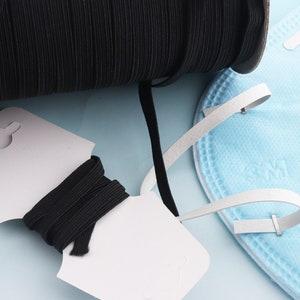 May include: A spool of black elastic cord with a white tag. The elastic cord is wound around the spool and is also shown on a white tag with a hole in the top. The elastic cord is used for making face masks.
