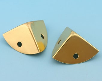 May include: Two gold corner protectors with rounded edges and two holes each. The protectors are made of metal and have a shiny finish.