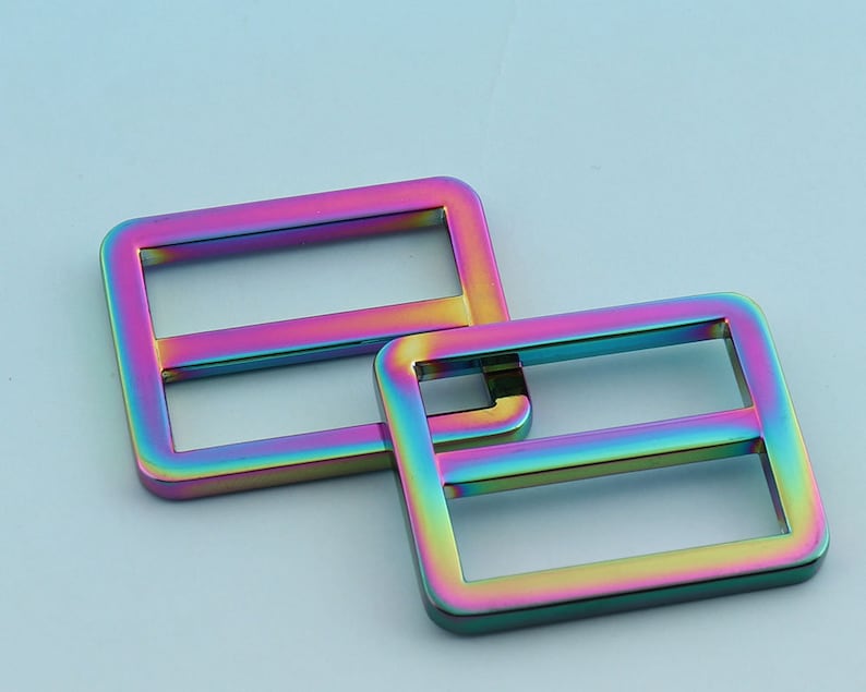May include: Two iridescent metal slider buckles, one larger than the other, with a rainbow finish. The buckles are made of metal and have a smooth, polished surface.