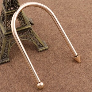 May include: A gold-toned metal bracelet with a rounded end and a pointed end. The bracelet is open and has a simple design.
