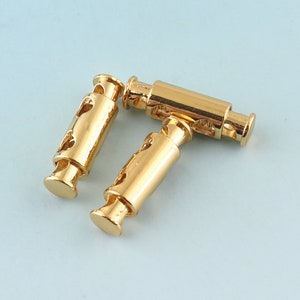 May include: Two gold-coloured metal cord ends with decorative cutouts. The cord ends are designed to be used with cords or ropes.