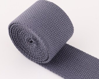 Könnte beinhalten: Eine Rolle graues gewebtes Baumwollband, eine Art strapazierfähiges Gewebe, das für Riemen, Gürtel und andere Anwendungen verwendet wird.