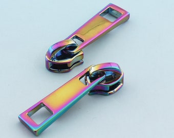 May include: Two iridescent zipper pulls with a rectangular slider and a metal loop. The pulls are a rainbow of colors, including pink, blue, green, and yellow.