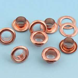 May include: A set of ten copper eyelets, some with a raised lip and some flat, for use in leather crafting or other DIY projects.