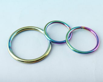 May include: Three iridescent metal rings of different sizes. The rings are a rainbow of colors, including blue, green, purple, and yellow.