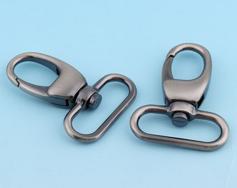 May include: Two silver-toned metal swivel clasps with a D-ring on one side and a hook on the other. The clasps are commonly used for attaching straps, leashes, or other accessories.