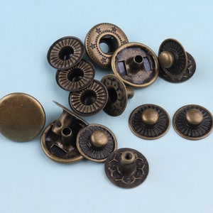 May include: A collection of antique gold-toned metal snap buttons with various designs. The buttons have a decorative, ornate look and are perfect for adding a vintage touch to clothing or crafts.