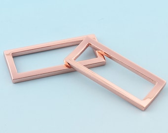 May include: Two rose gold metal rectangular frames. The frames are open and are stacked on top of each other.