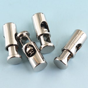 Puede incluir: Cuatro topes de cordón de metal plateado con un mecanismo de resorte. Los topes están diseñados para asegurar cordones y cables.