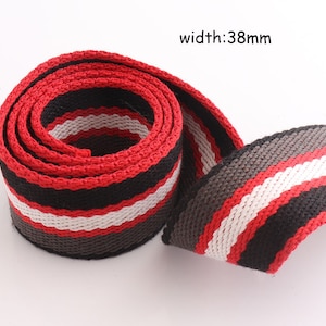 Pode incluir: Fita tecida em listras vermelhas, pretas, brancas e cinzas, com uma largura de 38 mm. A fita tem uma superfície texturizada.