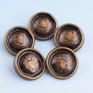 May include: Five antique-looking, round, bronze-coloured buttons with a square design in the centre.