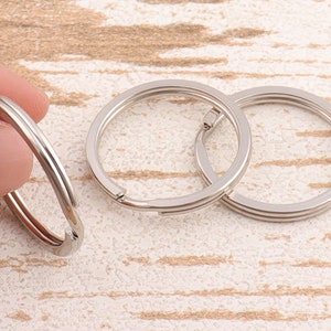 May include: Close-up of three silver-colored key rings. One ring is held by a hand, while the other two are lying flat. The rings are made of a shiny, metallic material and have a simple, functional design.