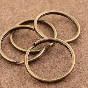 May include: Four antique gold-toned metal key rings. The rings are interlocked and arranged in a pile.