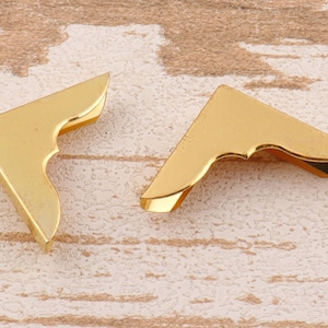 May include: Two gold metal corner protectors with a decorative scalloped edge.