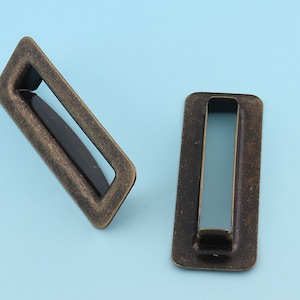 Könnte beinhalten: Zwei rechteckige Schubladengriffe aus antikem Goldmetall mit einem rechteckigen Ausschnitt in der Mitte.