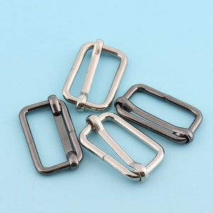 Puede incluir: Cuatro hebillas deslizantes de metal, dos plateadas y dos negras, para ajustar correas o cinturones.