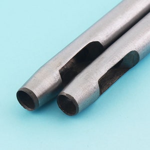 Può includere: Due punzoni in metallo dal design cilindrico. Gli strumenti hanno una finitura argentata e un'estremità cava e aperta per creare fori. Lo sfondo è azzurro chiaro.