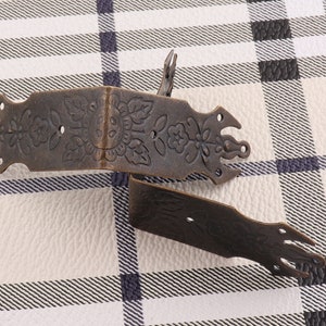 Puede incluir: Dos soportes de esquina de metal de estilo antiguo con un diseño floral. Los soportes son de metal oscuro con un acabado desgastado.