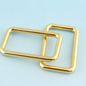 May include: Two gold-colored metal rings, one slightly larger than the other, are stacked on top of each other. The rings are smooth and have a polished finish.