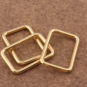 May include: Four gold-colored metal D-rings, stacked on top of each other. The rings are smooth and have a shiny finish.