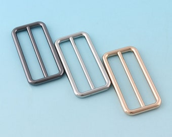 May include: Three metal slider buckles in different finishes: black, silver, and gold. Each buckle has a rectangular shape with a center bar.