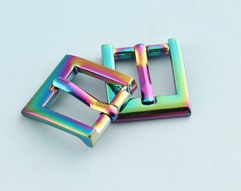 Op de afbeelding: Twee regenboogkleurige metalen gespen. De gespen zijn vierkant met een gladde, glanzende afwerking. De gespen zijn in een regenboog van kleuren, waaronder rood, oranje, geel, groen, blauw, indigo en violet.