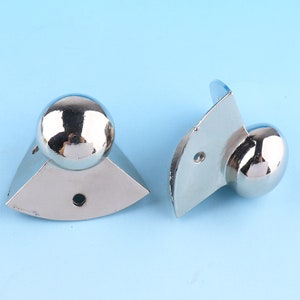 May include: Two silver corner protectors with a rounded ball shape on each end. The protectors are designed to protect furniture from damage.