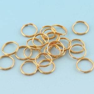 Könnte beinhalten: Ein Haufen goldfarbener Schlüsselringe aus Metall. Die Schlüsselringe sind alle gleich groß und gleich geformt und in einem zufälligen Muster angeordnet.