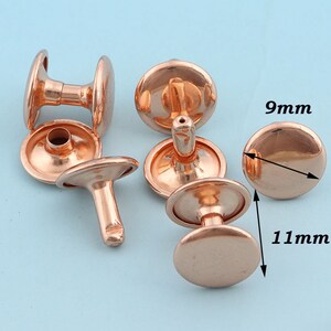Pode incluir: Cinco rebites de metal de cor cobre com cabeça abobadada e poste. Os rebites medem 9 mm de diâmetro e 11 mm de altura.