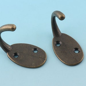 以下が含まれることがあります： 楕円形のベースと2つのネジ穴が付いたアンティークブロンズのフック2つ。フックは湾曲しており、滑らかな仕上げになっています。