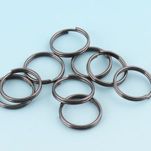 Op de afbeelding: Een set van acht zwarte metalen sleutelringen. De sleutelringen zijn allemaal even groot en hebben dezelfde vorm, en ze liggen in een losse stapel.