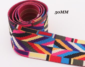 Könnte beinhalten: Eine Rolle farbenfroher, gemusterter Gurtbänder mit einem geometrischen Design in Rot-, Rosa-, Blau-, Gelb- und Schwarztönen. Der Text "50MM" ist sichtbar, was die Breite des Gurtbandes angibt. Das Gurtband ist eng gerollt und zeigt das Muster. (5 cm)