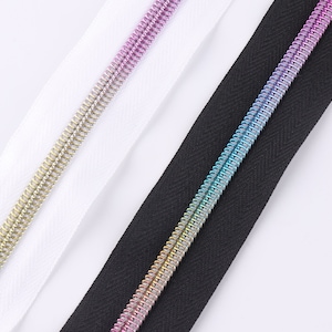 Peut inclure: Trois bandes de fermeture éclair avec des dents métalliques de différentes couleurs. Les bandes sont blanches, noires et dégradées de rose, bleu et vert.