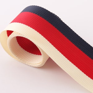 Peut inclure: Un ruban rayé blanc, rouge et bleu marine. Le ruban est enroulé et les rayures sont visibles.